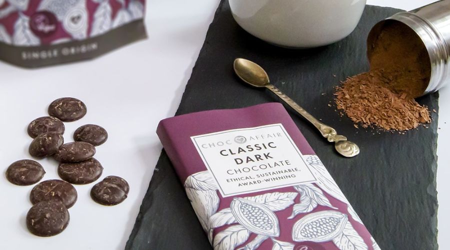 A bar of dark chocolate next to chocolate buttons and hot chocolate powder