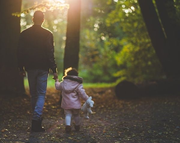 Father holding his young daughter's hand whilst walking through the woods